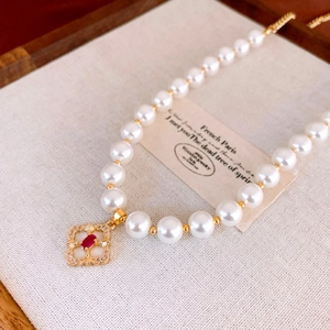 Detailed macro view of gold-plated flower pendant with red gemstone and pearls