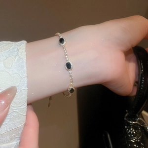 Macro detail of oval black gemstone bracelet with gold chain and zircon inlay