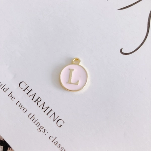 Detailed view of a round pink enamel pendant with gold-trimmed letter L on vintage paper
