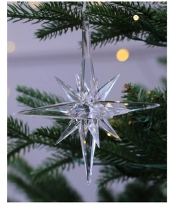 Close-up of a clear acrylic snowflake ornament hanging on a Christmas tree with warm lights