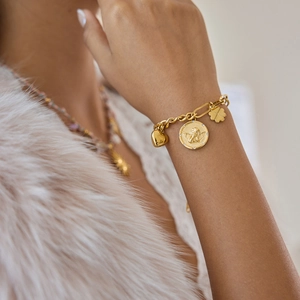 Gros plan d'un bracelet à maillons dorés avec breloques cœur, pièce d'ange et trèfle