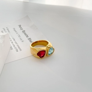 Detail of 18K gold heart-shaped ring with red and blue zircon on a minimalist white background