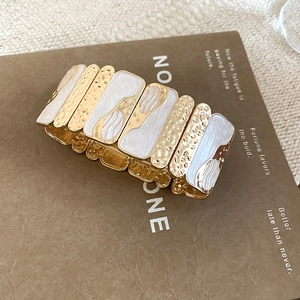 Detail of wide stretch bracelet featuring hammered gold finish and white marble enamel inserts