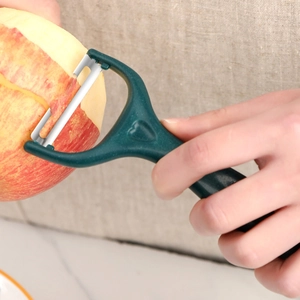 Green stainless steel peeler for fruits and potatoes with ergonomic handle being used on apple