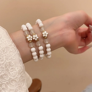 Close-up of a three-piece set of white beaded bracelets with gold enamel flower charms