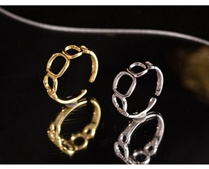 Macro shot of geometric hollow square rings in gold and silver over black reflective surface