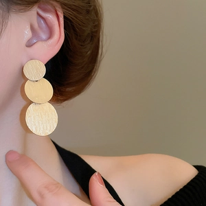 Macro detail of three-tier brushed gold geometric circular drop earrings on a model