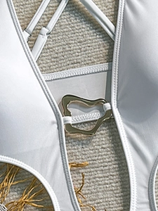 Detail of white swimsuit featuring a unique gold metal buckle and adjustable straps