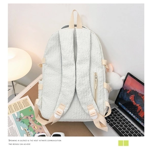 Détail d'un sac à dos plissé crème avec une breloque lapin en peluche sur un bureau