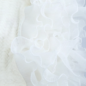 Detail of white textured fabric with layered mesh ruffles and pleated dress material