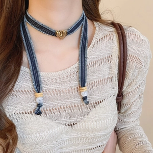 Macro detail of denim fabric choker with golden 3D heart pendant and wooden beads