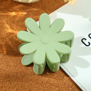 Matte light green daisy flower hair claw clip on a minimalist cork and book background