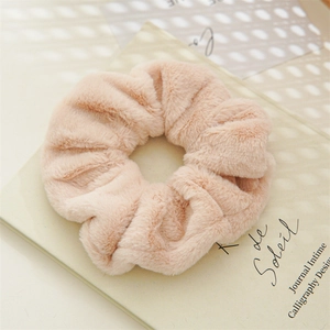 Close-up of soft beige faux rabbit fur scrunchie on a book page with gentle lighting