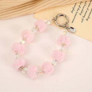 Pink plush ball and faceted bead phone charm with silver metal clasp on warm background