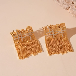 Detail of gold fringe earrings with zircon stones on a decorative stone background