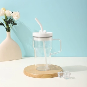 Close-up of a clear glass water bottle with white handle and straw on a wooden coaster