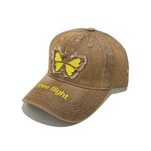 Detail view of brown washed denim baseball cap with yellow butterfly patch and embroidery