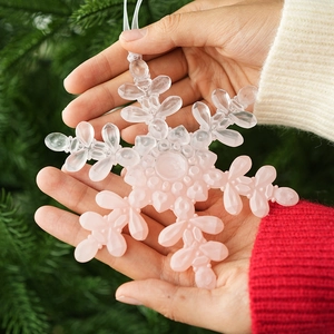 Pink gradient snowflake Christmas tree ornament held in hands with festive background