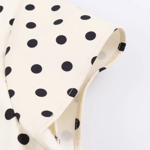 Close-up of black polka dot fabric on a cream dress showing detailed stitching and texture