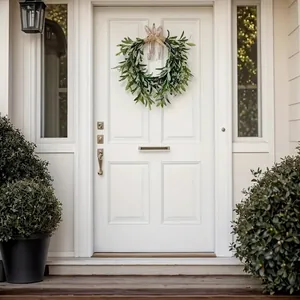 Artificial olive leaf wreath with burlap bow decoration on white front door