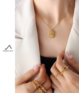 Close-up of golden stainless steel square pendant and rings styled on a model