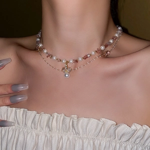 Detailed view of layered necklace featuring crown pendant, pearls, and pink crystals on skin