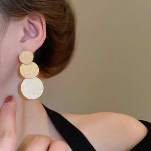 Macro side view of golden brushed metal triple disc drop earrings on a model