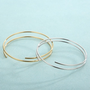 Macro shot of minimalist gold and silver double-layered open bangles on blue background