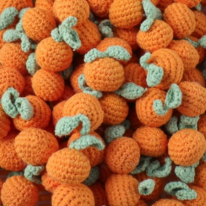 Close-up of handmade knitted orange pendants with green leaves in a stacked arrangement