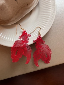 Detailed macro view of red koi fish earrings with hollow metal craft on a white plate