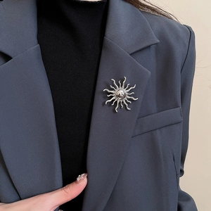 Silver sunburst brooch with wavy rays on a grey blazer lapel for high-end fashion styling