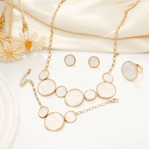 Golden jewelry set with white marble discs on white silk featuring necklace and ring