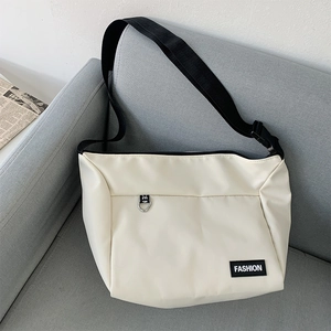 Detail of a white crossbody bag featuring a FASHION woven label on a gray sofa