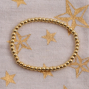 Elegant gold-plated beaded elastic bracelet displayed on a textured beige fabric background
