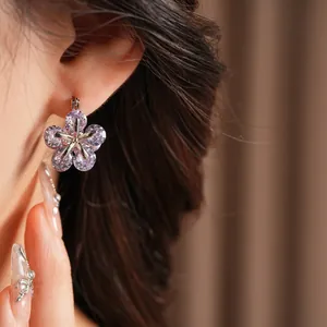 Boucles d'oreilles fleurs avec zircons violets portées sur l'oreille sur fond marron