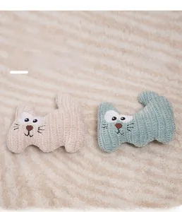 Detailed view of hand-knitted cat plush toys with embroidered faces on a soft fabric base