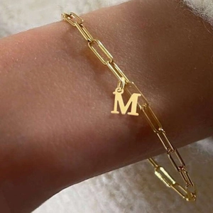 Macro shot of a gold paperclip chain bracelet featuring a letter M pendant on a wrist