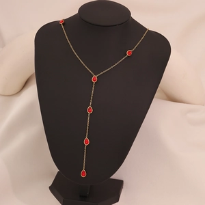 Macro detail of gold Y-necklace featuring elegant red teardrop glass charms on a black bust