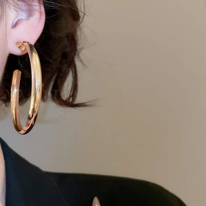 Close-up of a model wearing large polished gold geometric hoop earrings with a metallic finish