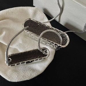 Collier chic avec pendentif mini sac tressé argenté sur une pochette en tissu crème