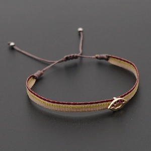 Close-up of woven cord bracelet with gold lip pendant and inlaid red gemstone