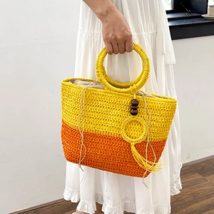 French straw tote bag with bow detail and tassels held by woman in a white dress