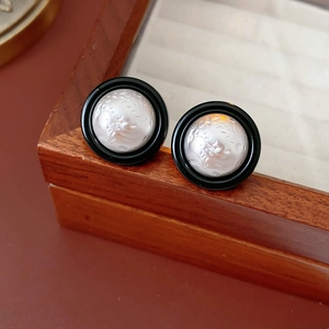 Detailed close-up of retro button-style earrings with black enamel and white pearl texture