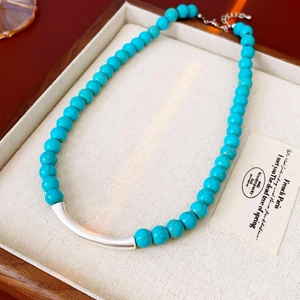 Détail du collier ethnique en perles de turquoise avec tube métallique incurvé poli argenté