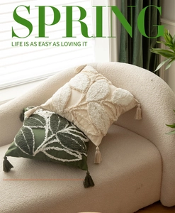 Detail of embroidered daisy throw pillows with tufted leaf patterns and tassels on a sofa