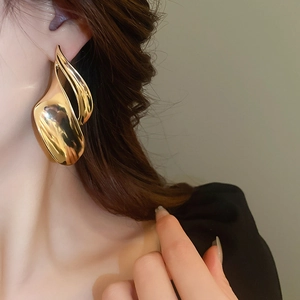 Close-up of model wearing chunky abstract fluid gold earrings with high metallic luster