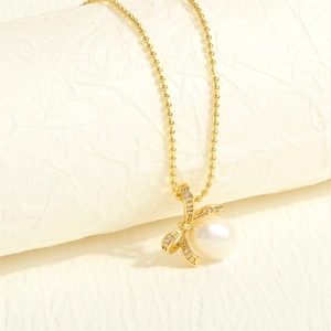 Macro detail of a golden bow pendant with small diamonds and a round freshwater pearl