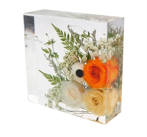 Macro shot of preserved orange roses and white flowers inside a clear resin cube