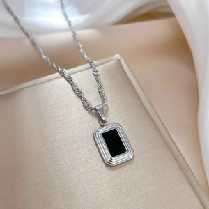 Macro shot of minimalist silver square pendant necklace with black inlay on silk fabric