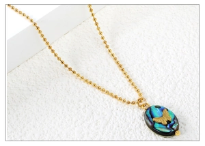 Detail of golden bead chain and oval abalone shell pendant with a butterfly motif